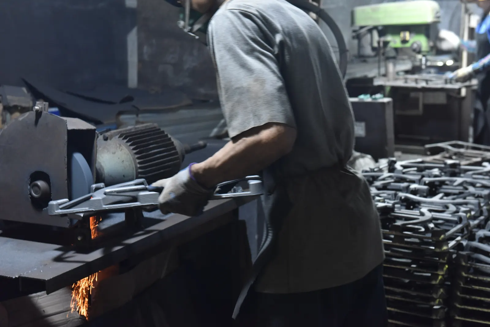 Operator grinding or finishing a cast iron part with visible sparks in a workshop